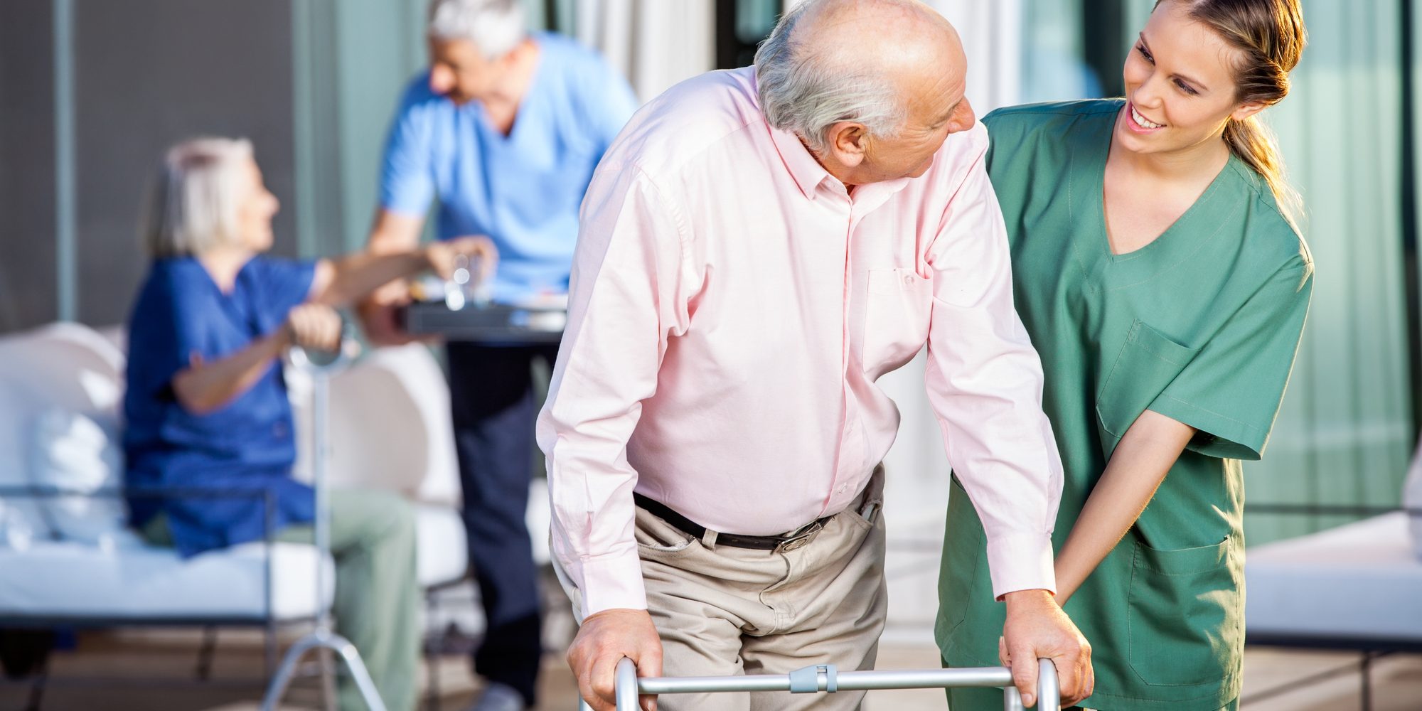 Happy female caretaker assisting senior man in using Zimmer frame at nursing home yard